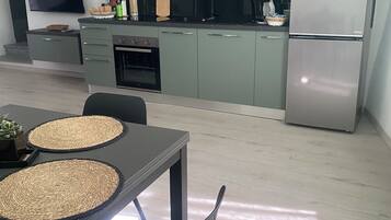 Een moderne keuken met grijze kastjes, een roestvrijstalen koelkast en een flatscreen televisie aan de wand.