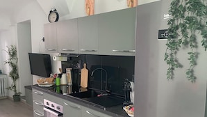 Eine moderne Küche mit grauen Schränken, einem Edelstahlkühlschrank, einem Einbauofen und einem Flachbildfernseher.