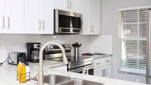 Une cuisine moderne équipée d’appareils électroménagers en acier inoxydable, d’un évier à deux bacs et d’une fenêtre avec des stores.