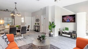 A modern living room with a dining area, a staircase, and a TV mounted on the wall. - Bella Vida Family Escape Near Disney (Kissimmee)