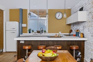 A modern kitchen with a central island, white cabinetry, and a brick accent wall. - Stylish Hove Mews | Close to Beach & Station - Pass the Keys (Hove)
