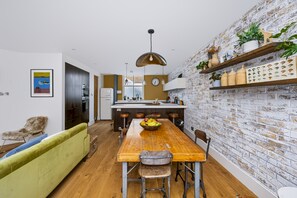 A modern kitchen with a wooden dining table, bar stools, and a brick wall. - Stylish Hove Mews | Close to Beach & Station - Pass the Keys (Hove)