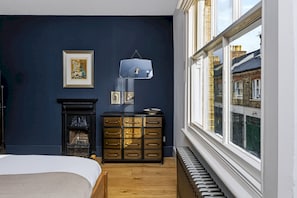 A bedroom with a bed, dresser, fireplace, and a view of the outside through a window. - Stylish Hove Mews | Close to Beach & Station - Pass the Keys (Hove)