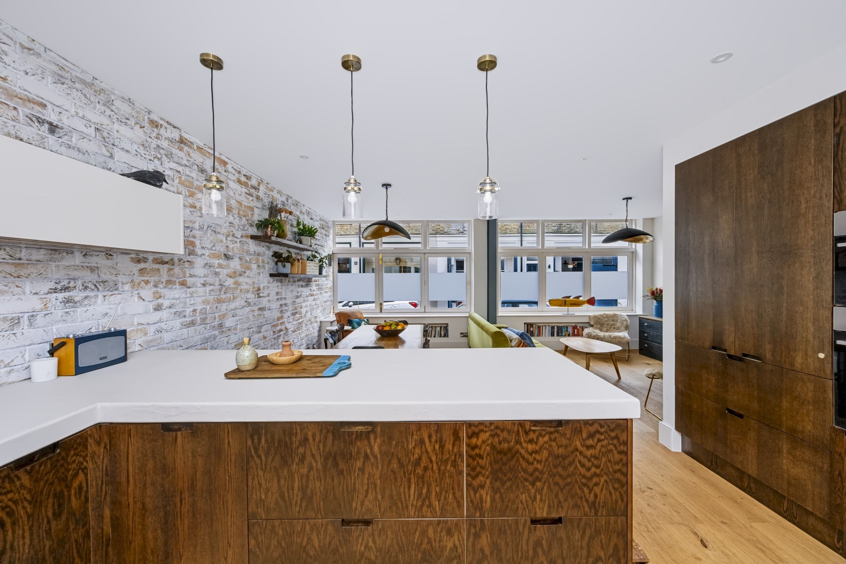 A modern kitchen with a white island, wooden cabinets, and pendant lighting.