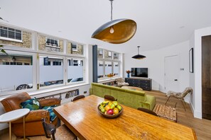 Une cuisine moderne avec une table à manger en bois, un saladier de fruits et une vue sur l’extérieur.