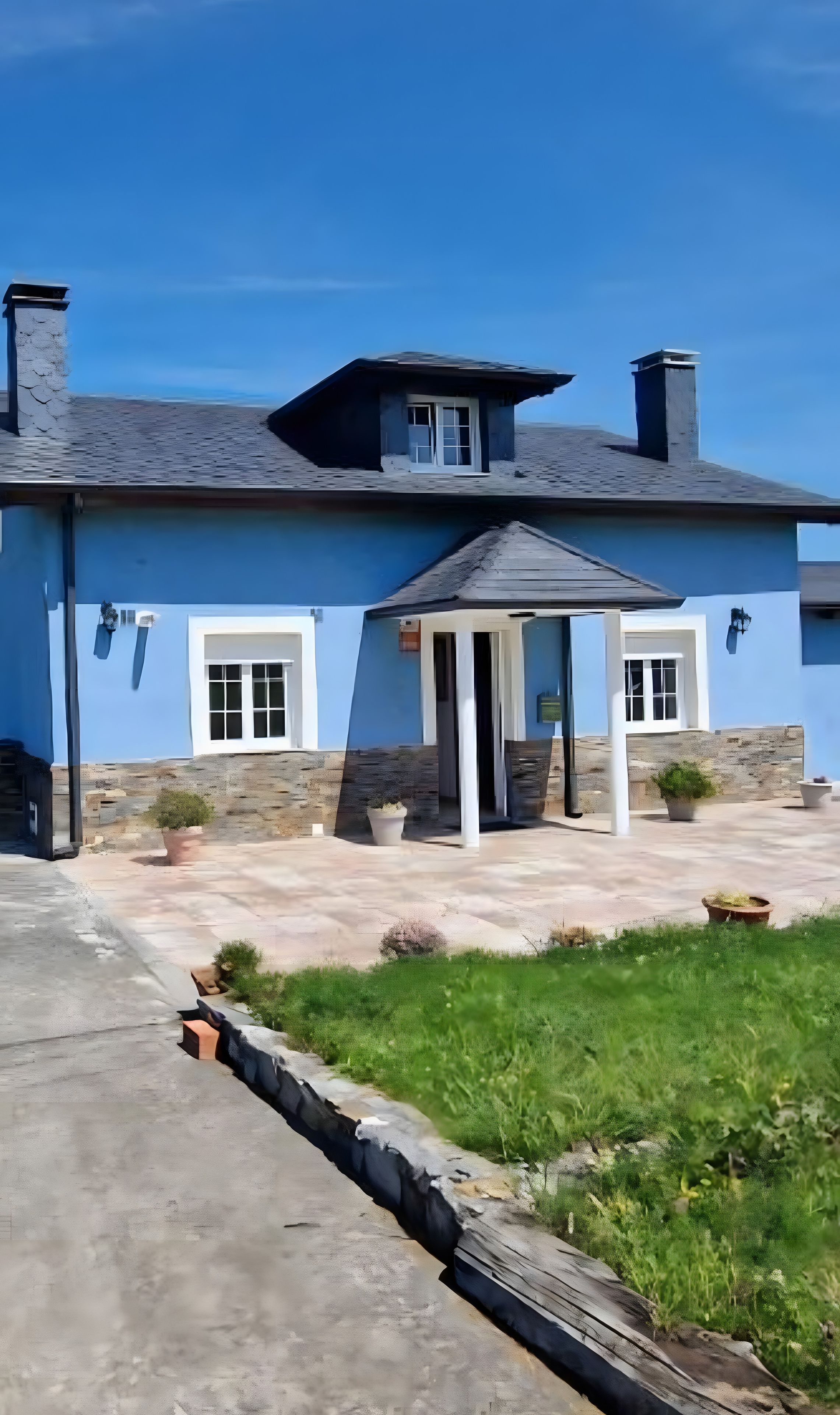 A blue building with a stone facade, a covered porch, and a clear sky.