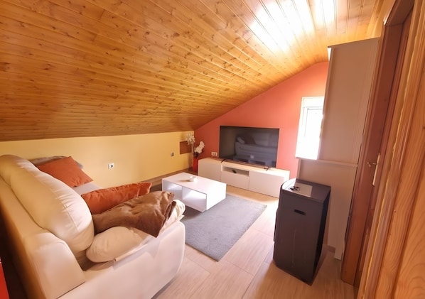 A cozy living room with a sloped ceiling, a sofa, a coffee table, a TV, and a small cabinet. - Casa Azul: mountain views, private terrace, and Wi-Fi (Quintana)