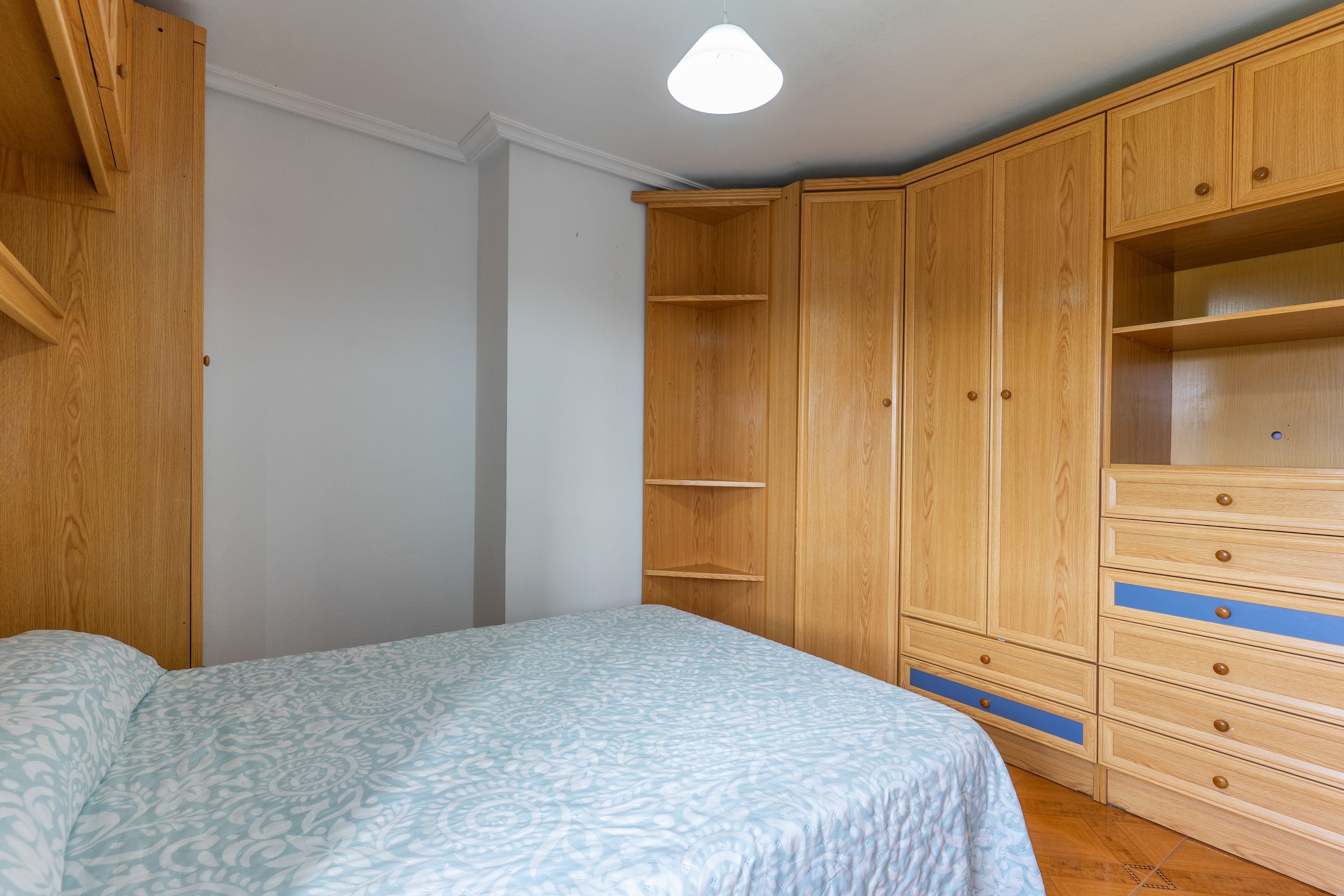 Ein Schlafzimmer mit Bett, Holzschrank und Deckenleuchte.