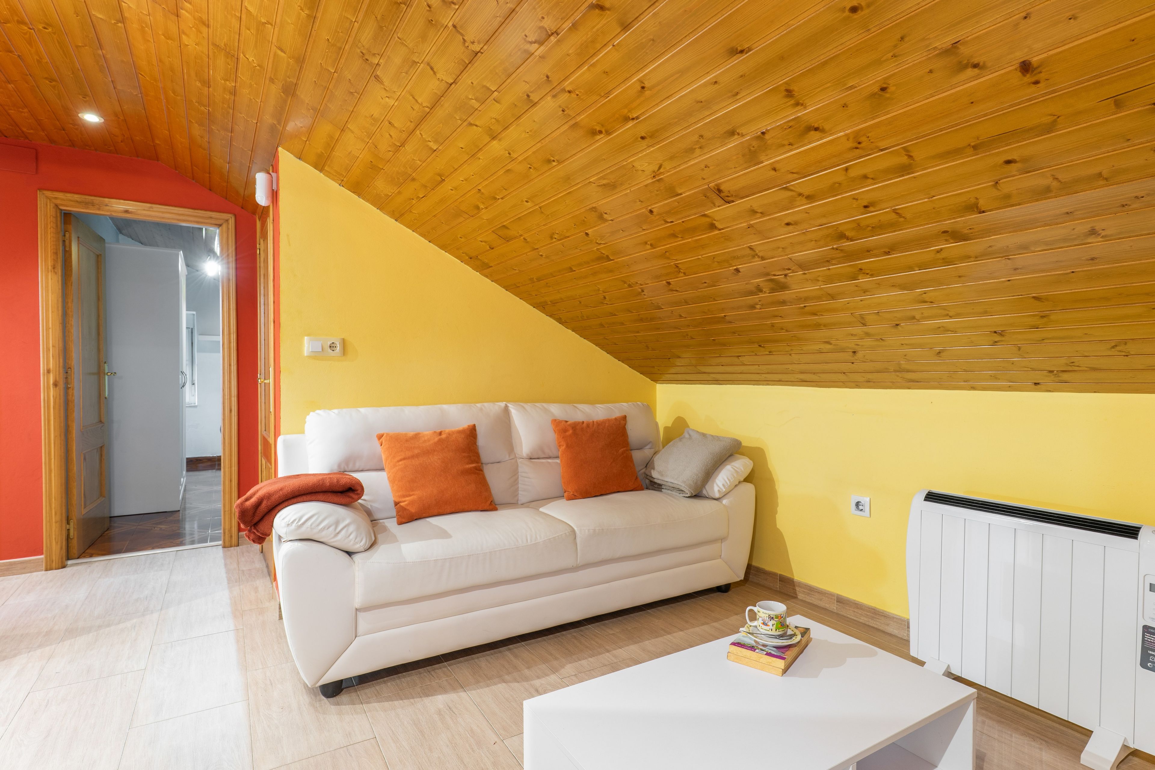 Een woonkamer met een witte bank, oranje kussens, een witte salontafel en een radiator.