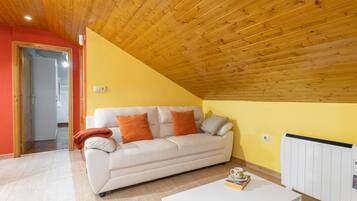 Een woonkamer met een witte bank, oranje kussens, een witte salontafel en een radiator.