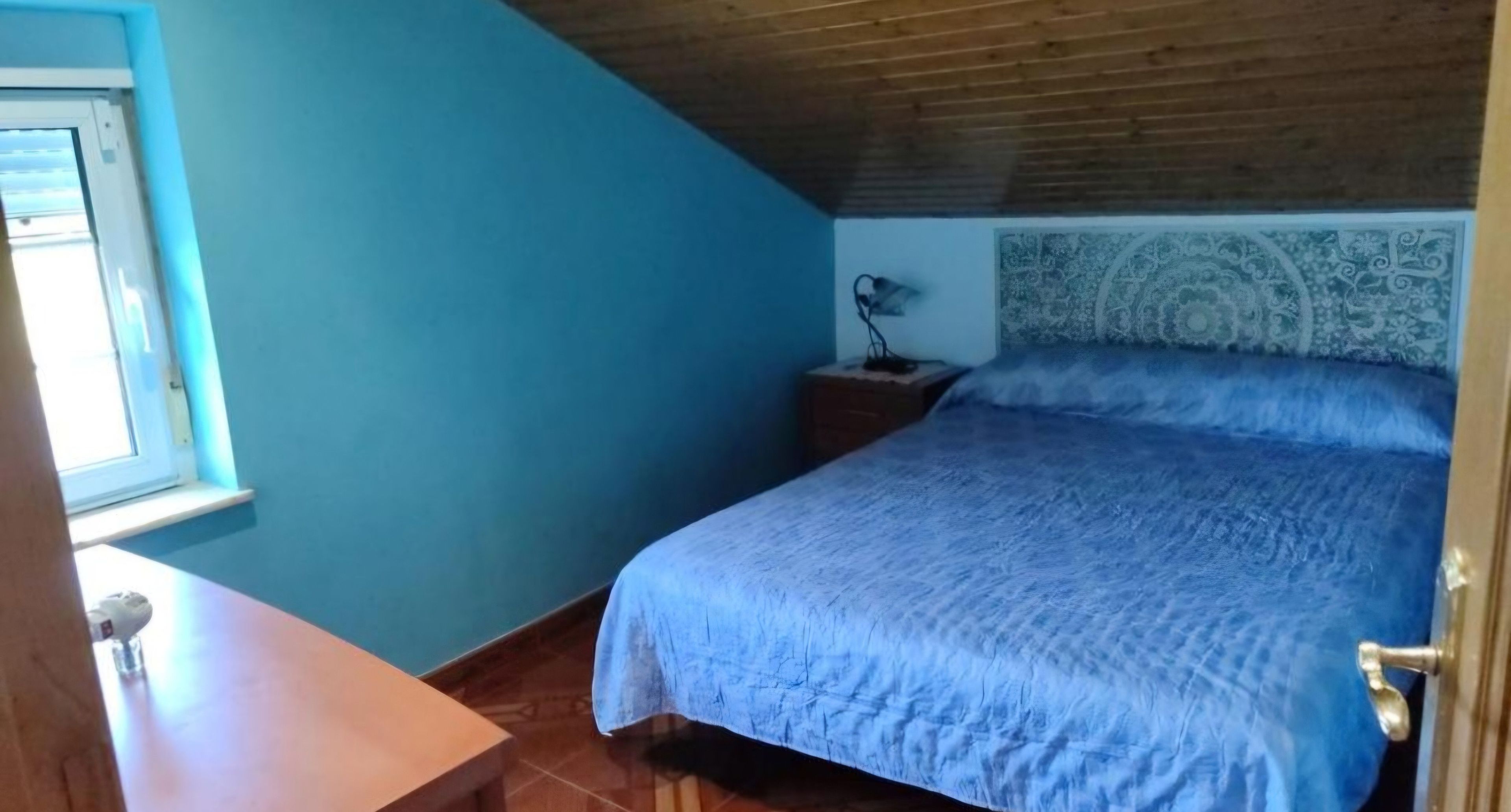 Un dormitorio con cama, mesita de noche, lámpara y ventana.