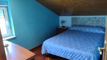 Un dormitorio con cama, mesita de noche, lámpara y ventana.