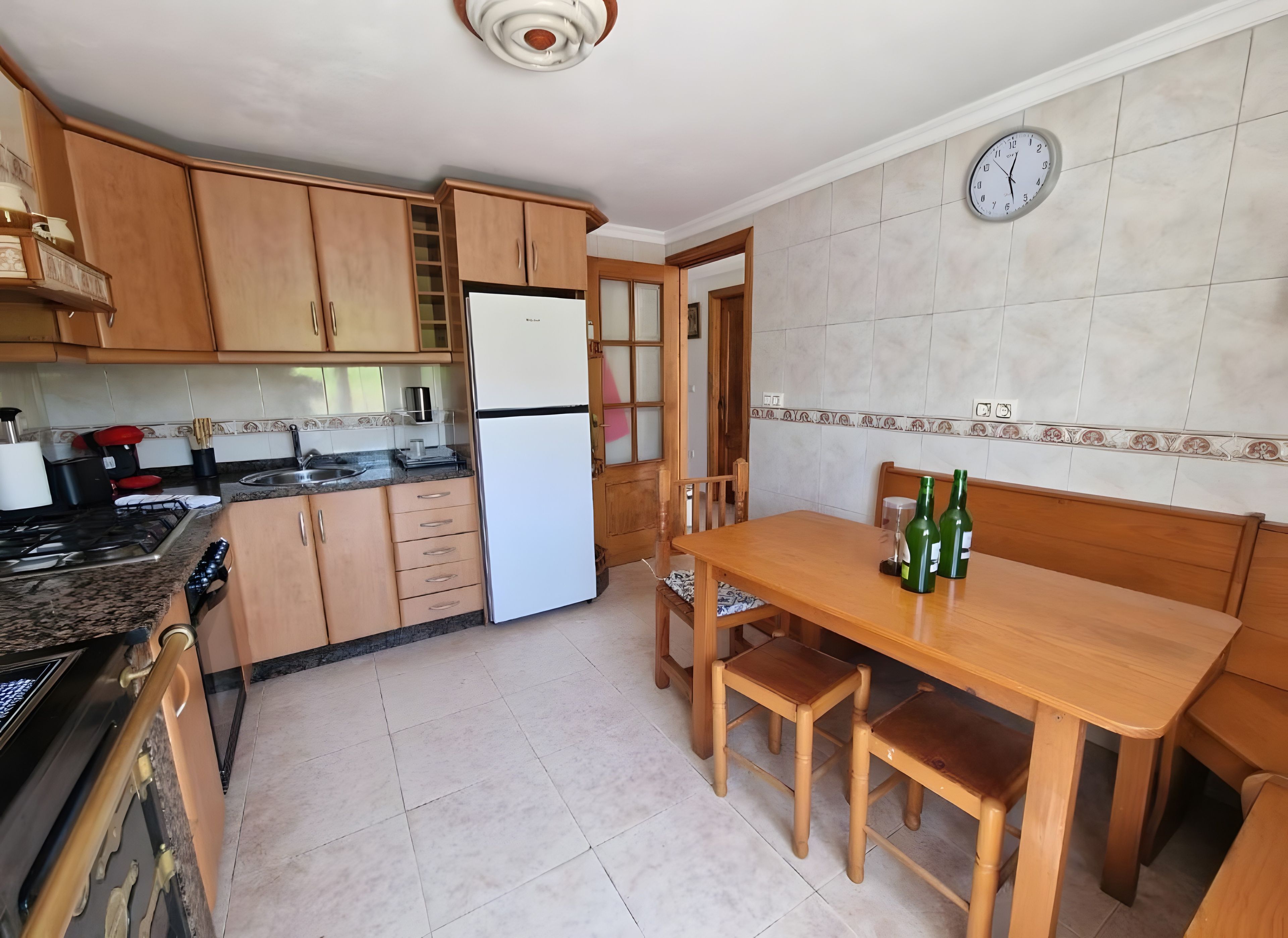 Une cuisine avec des meubles de rangement en bois, un réfrigérateur, une cuisinière, un évier et une table à manger avec des chaises.