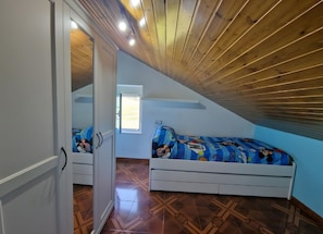 A bedroom with a sloped ceiling, a bed with a cartoon-themed bedspread, a small window, and a door leading to another room. - Casa Azul: mountain views, private terrace, and Wi-Fi (Quintana)