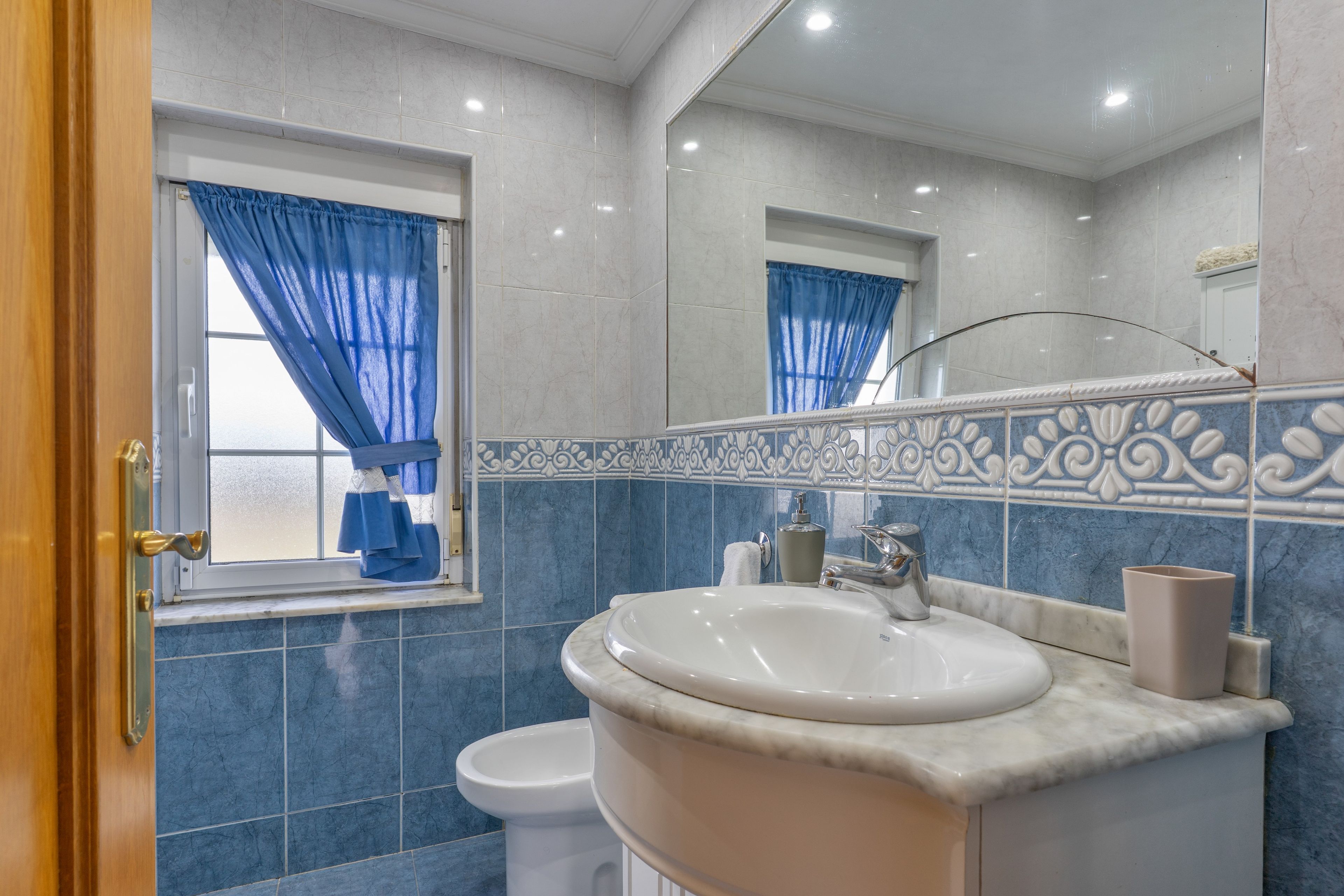 Un baño con lavamanos blanco, espejo y paredes de azulejos azules.