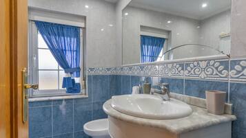 Un baño con lavamanos blanco, espejo y paredes de azulejos azules.