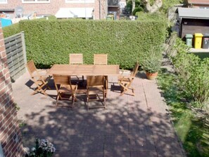 A wooden table and chairs set on a paved patio with a hedge in the background. - Holiday Home With 2 Bedrooms (Wyk auf Foehr)