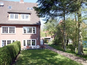 Ein zweistöckiges Backsteinhaus mit befestigter Auffahrt, Rasenfläche und kleiner Terrasse mit Gartenmöbeln.