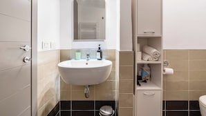A bathroom with a white sink, a mirror above it, a towel rack, and a shelf with toiletries. - Charming Apt in the Heart of Florence (Firenze)