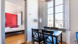 A room with a bed, a dining table with chairs, a window with a view of buildings, and a red wall. - Charming Apt in the Heart of Florence (Firenze)