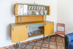 Ett skåp i vintage-stil med glasdörrar, en blå stol och ett golv med mönstrade plattor.