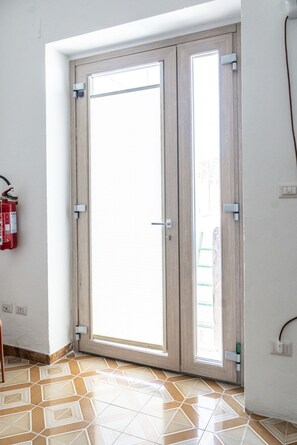 Una habitación con un amplio ventanal corredera, un extintor de incendios sujeto a la pared y suelo de baldosas.
