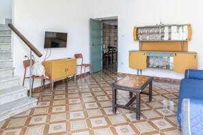 Ein Zimmer mit Fliesenboden, einer Couch, einem kleinen Tisch, einem Schrank, einem Fernseher und einer Treppe.