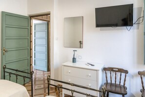Ein Zimmer mit einem Bett, einem Schreibtisch mit Schubladen, einem Sessel, einem an der Wand montierten Fernseher und einer grünen Tür.