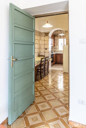 Un pasillo que conduce a un comedor con suelo de baldosas, una mesa con sillas y una cocina al fondo.