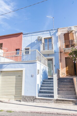 Un edificio de dos pisos con fachada blanca, un balcón y una escalera que conduce a la entrada.