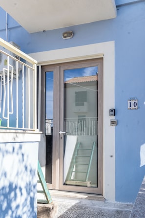 Um edifício residencial com fachada azul, porta de madeira e varanda com grade de metal.