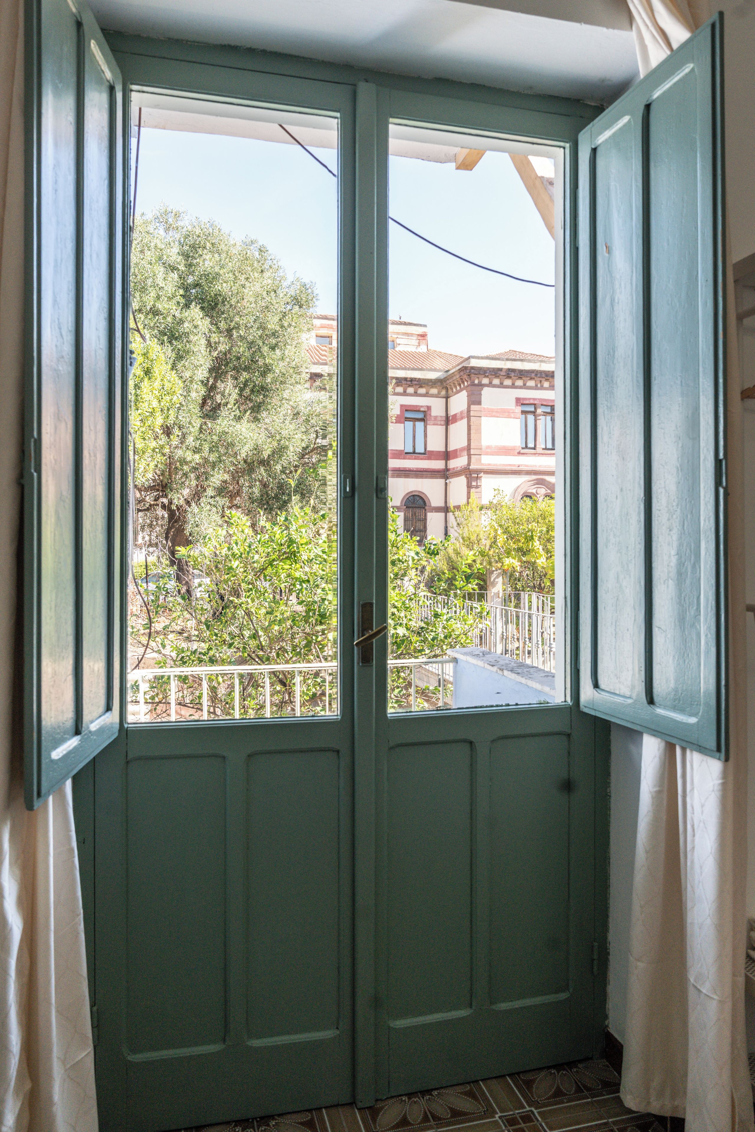 A room with a green door and a view of a tree and buildings outside.