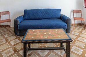 Ein Zimmer mit einem blauen Sofa, zwei Holzstühlen und einem Tisch mit Blumenmuster.