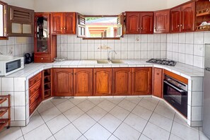A kitchen with wooden cabinets, a white countertop, a sink, a stove, and a microwave. - Maison Bois Jadé - Proche de La Trinité (Arrondissement of La Trinité)