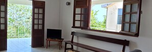 A room with a TV on a small table, a bench, and a window with a view of greenery. - Maison Bois Jadé - Proche de La Trinité (Arrondissement of La Trinité)