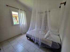 Ein Schlafzimmer mit einem Himmelsbett, einem Fenster mit Vorhängen und einem Fliesenboden.