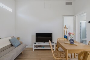 A modern living room with a flat-screen TV, a sofa, a dining table with chairs, and a bookshelf. - La Petite Cabane - Proche gare et plage (Arcachon)