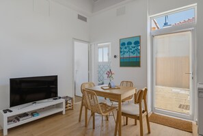 A modern living room with a flat-screen TV, a dining table with chairs, and a large window. - La Petite Cabane - Proche gare et plage (Arcachon)