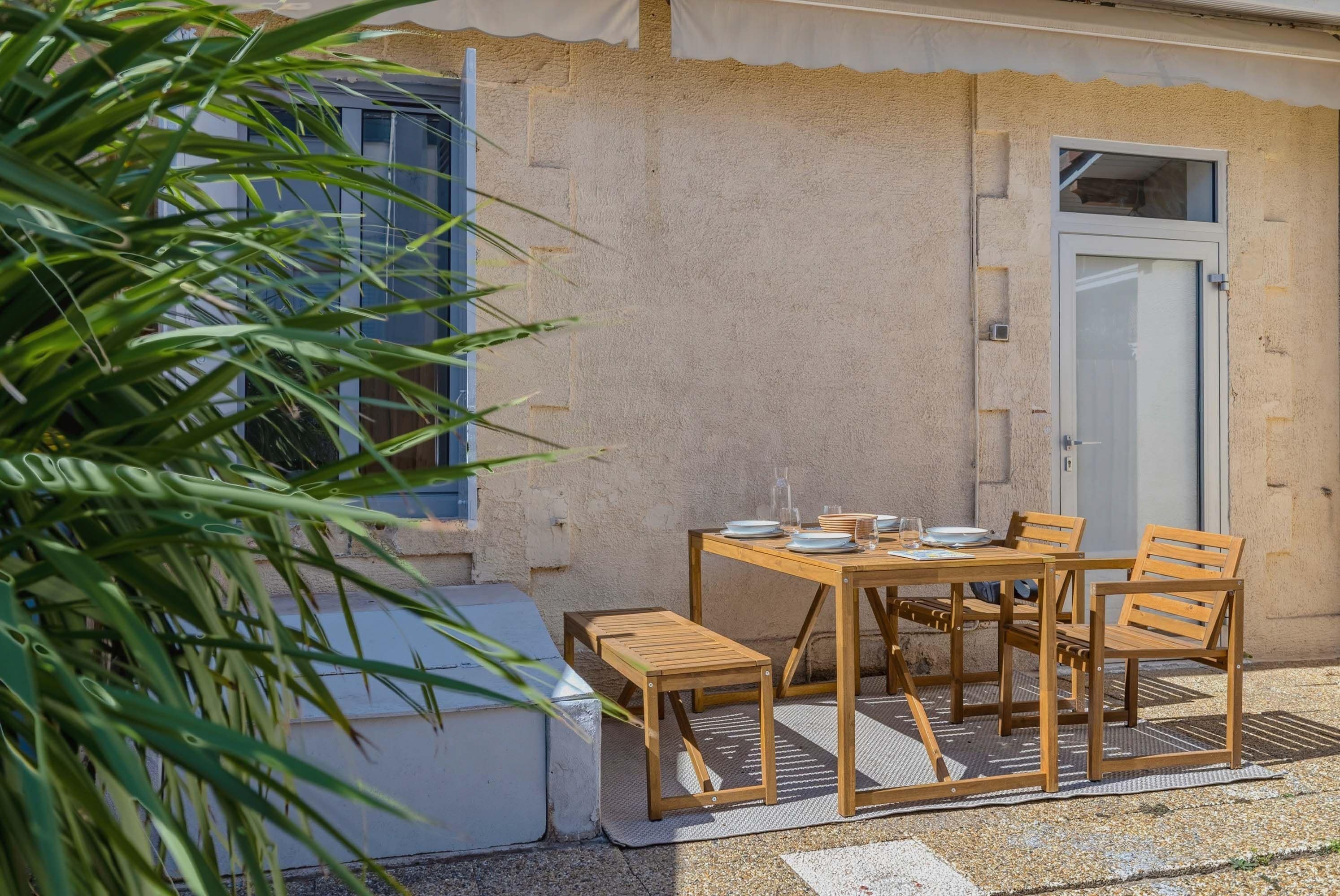 Una mesa de madera al aire libre con sillas, una puerta y una ventana con persianas.