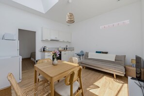 A modern kitchen with white cabinets, a dining area with a wooden table and chairs, and a grey sofa in a living room. - La Petite Cabane - Proche gare et plage (Arcachon)