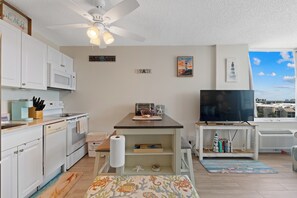 A compact living space with a kitchenette, a dining area, a television, and a view of the cityscape. - 🏖️ Estero Beach 802C Beach Sunrise | Beach Front Condo | Pool and Tennis🎾 (Fort Myers Beach)
