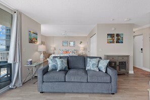 A modern living room with a grey sofa, a dining area, and a view of a balcony. - 🏖️ Estero Beach 802C Beach Sunrise | Beach Front Condo | Pool and Tennis🎾 (Fort Myers Beach)