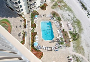 Ein Luftbild eines Hotels mit einem zentral gelegenen Schwimmbad, umgeben von Liegestühlen und einem Strandbereich.