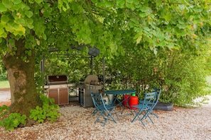 An outdoor patio with a grill, seating, and a tree providing shade. - Les Rouazes - Demeure pour 15p (Mareuil-lès-Meaux)