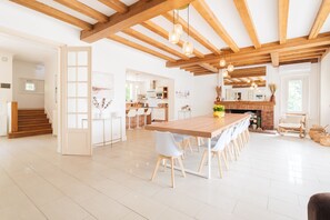 A spacious kitchen with a large wooden table, white chairs, and a brick fireplace. - Les Rouazes - Demeure pour 15p (Mareuil-lès-Meaux)
