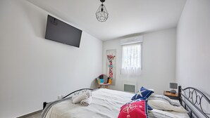En pænt redt seng med hvide dyne og rød pude med et kompasmotiv, et natbord med lampe og en stol med farverige pude.