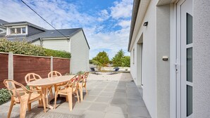 En terrasse med et bord og stole, et træhegn og et hus med hvide facader.