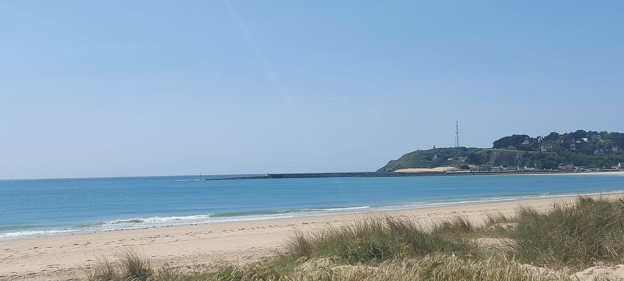 A beach with a clear sky, a sandy shore, and a distant hill with buildings.