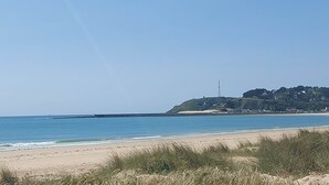 En strand med klart skys og sandet bred, samt en fjern bakke med bygninger.