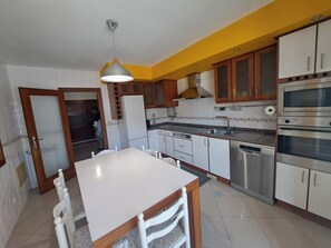 A kitchen with white cabinets, a stainless steel oven, and a dining table with chairs. - Cozy 2-Bedroom Apartment in Praia da Vagueira (Praia da Vagueira)